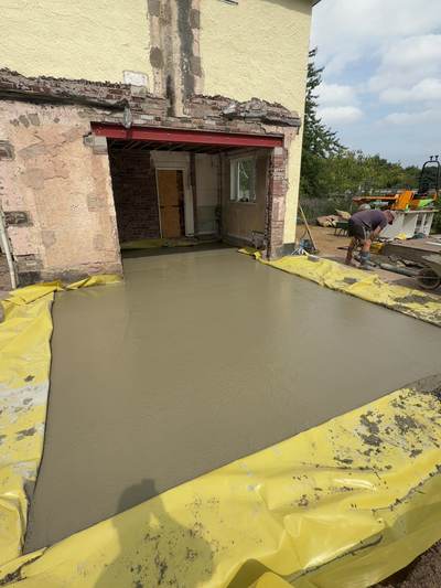 Freshly poured house extension floor slab over yellow DPM, tied into the existing house where the rear wall has been opened up beneath a new red steel beam