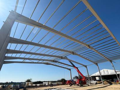 Steel portal frame and purlins erected against a blue sky, with further steel members laid out ready