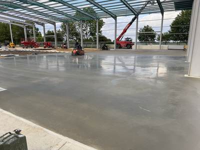 Operator power-floating a large concrete floor slab inside the steel frame