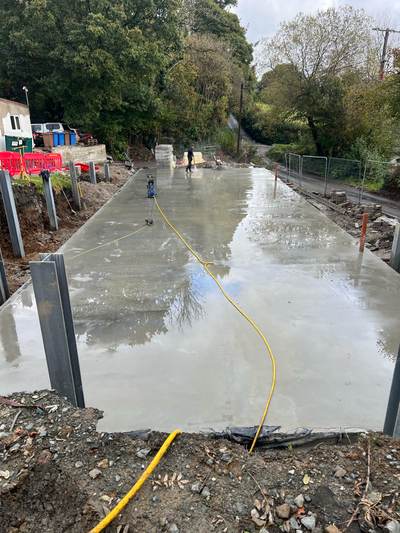 Freshly poured concrete slab being finished, with the steel retaining wall posts standing along its edge