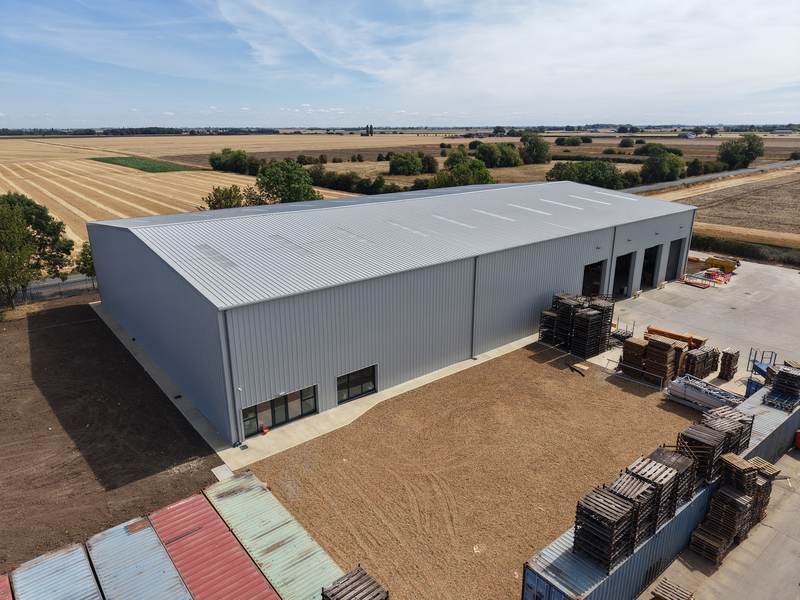 A completed steel-framed industrial building with profiled metal cladding, roller-shutter doors and a concrete yard, seen from above