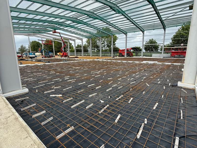 Steel reinforcement mesh on spacers laid over a membrane inside a steel-framed building, ready for the concrete pour
