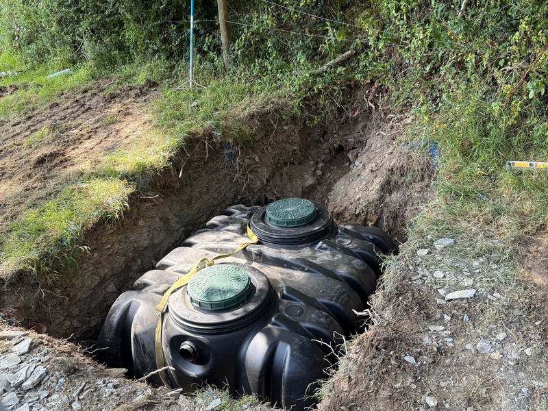 A new septic tank set in its excavation at the edge of a field, ready for backfilling